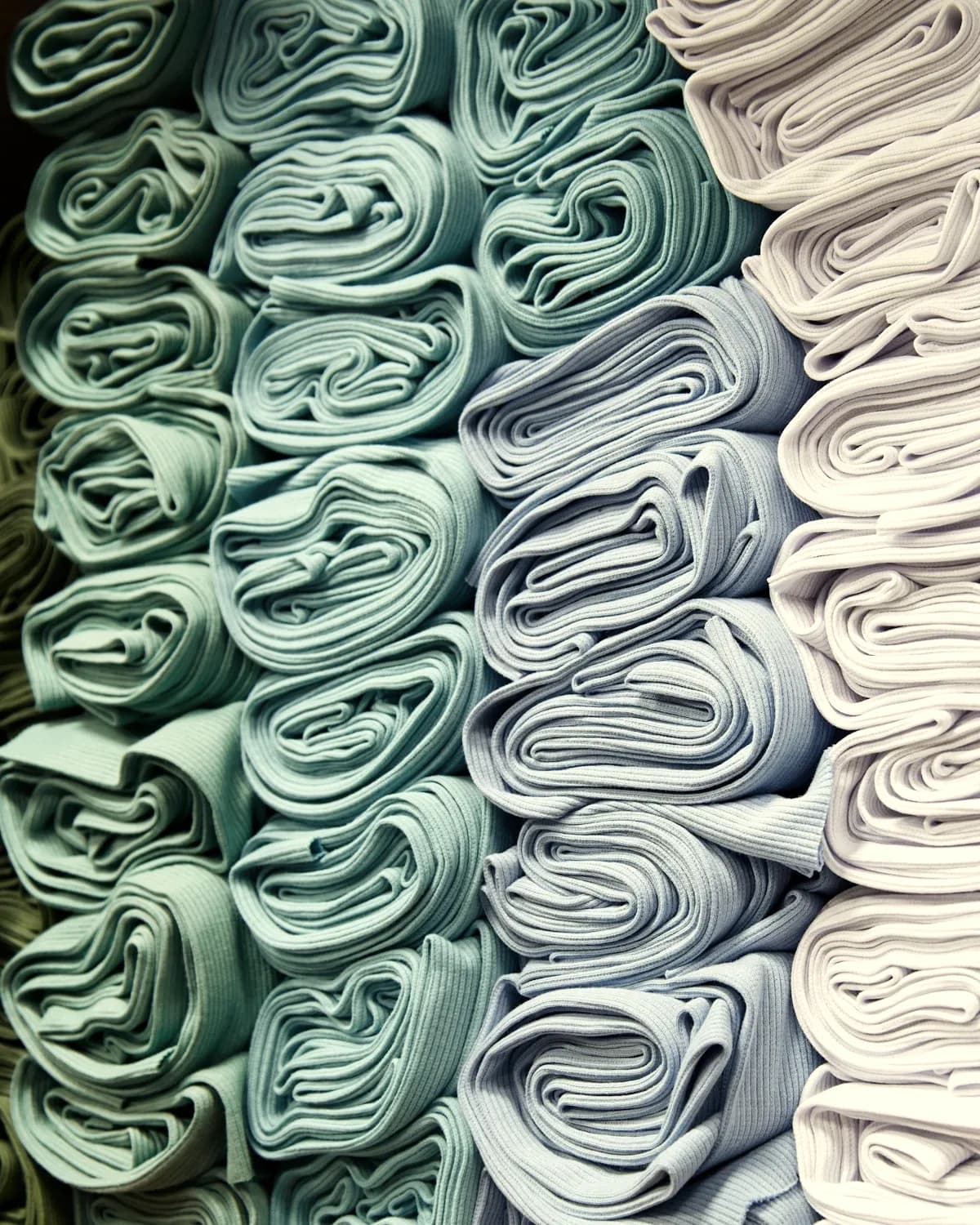 Rouleaux de tissus rangés par nuances de bleu, de vert et d'écru.